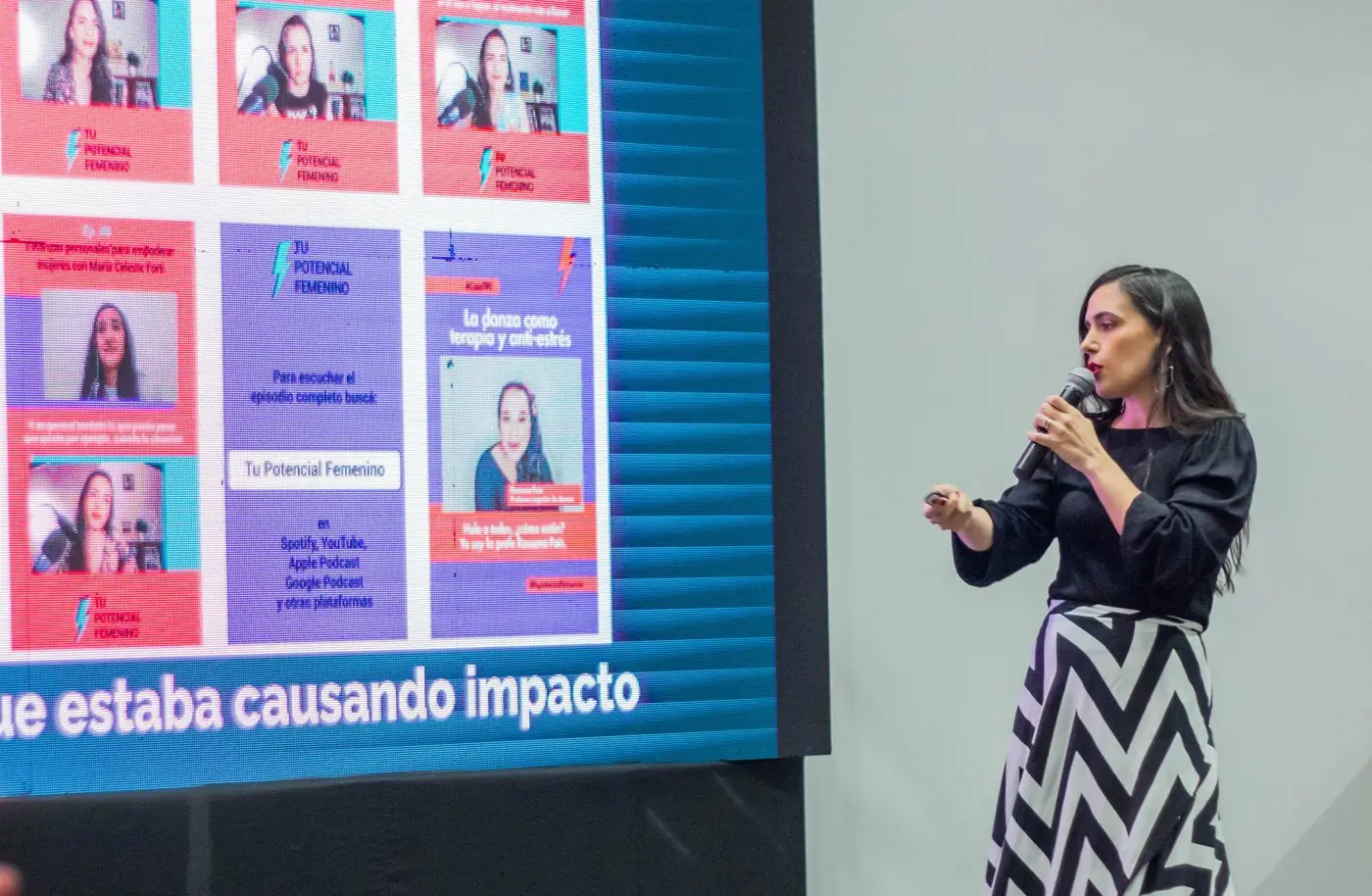 Aura da una charla con micrófono frente a una pantalla con publicaciones de redes sociales