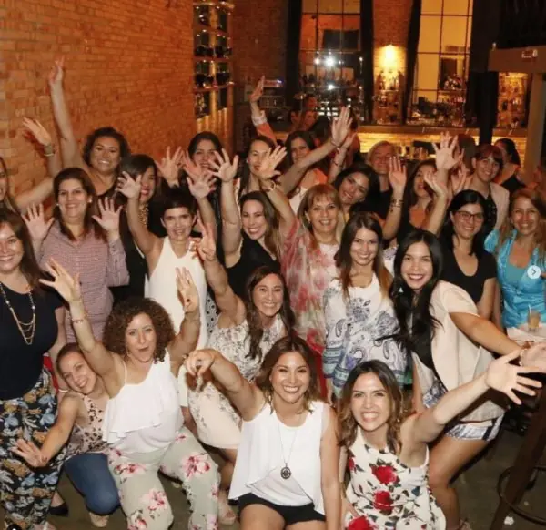 Un grupo grande de mujeres sonríe y saluda con las manos en alto en un encuentro