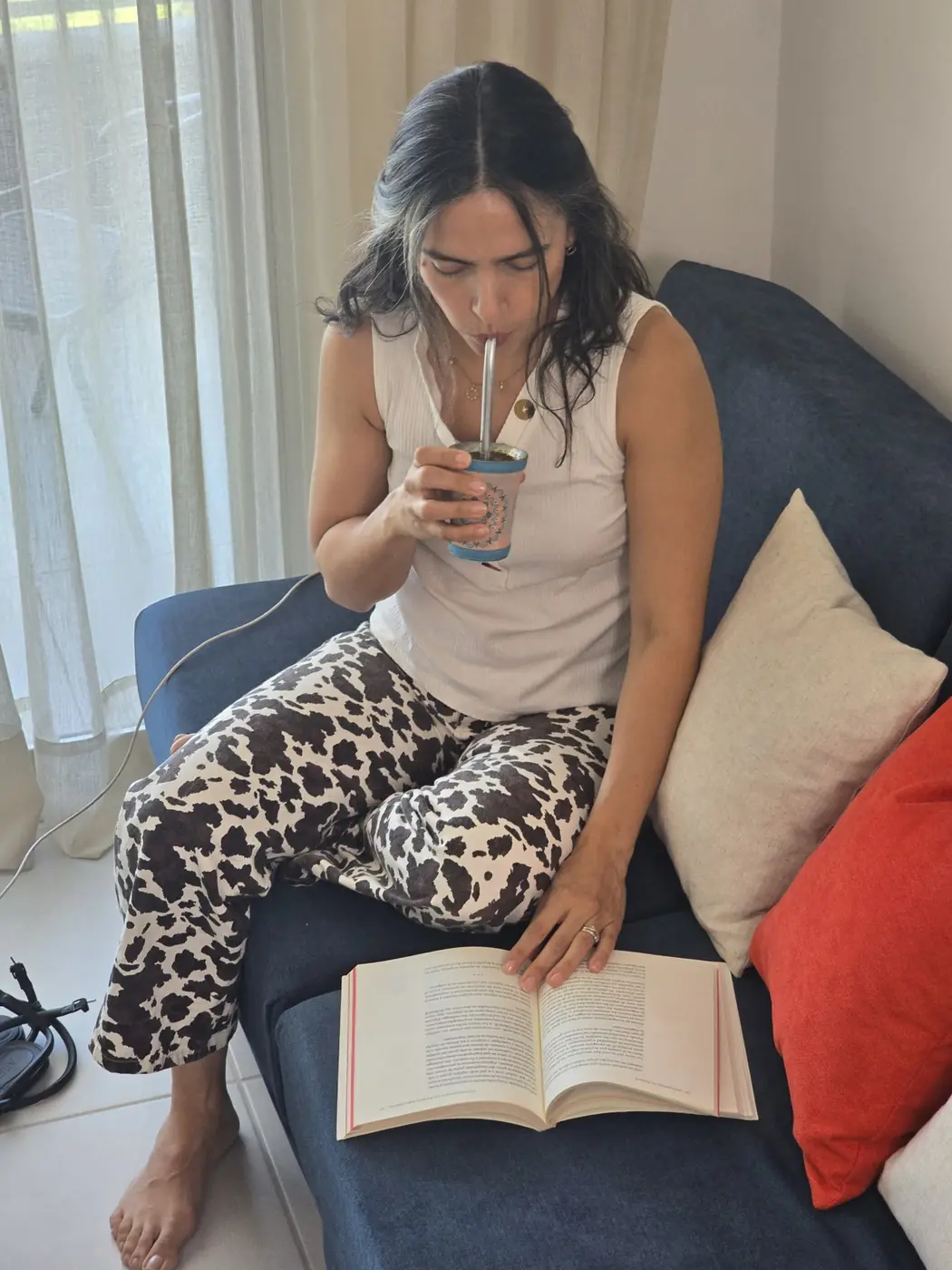 Aura toma tereré en el sillón de la sala, con un libro abierto
