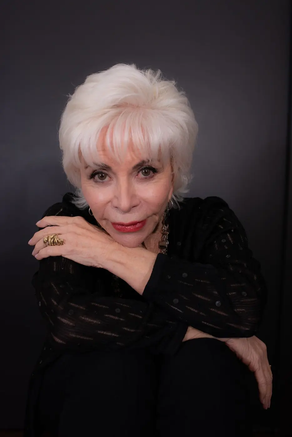 Isabel Allende, de negro, apoya el mentón sobre el brazo y mira a cámara