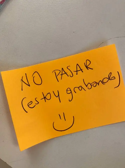 Un papel naranja pegado en la puerta dice «No pasar (estoy grabando)» con una carita sonriente